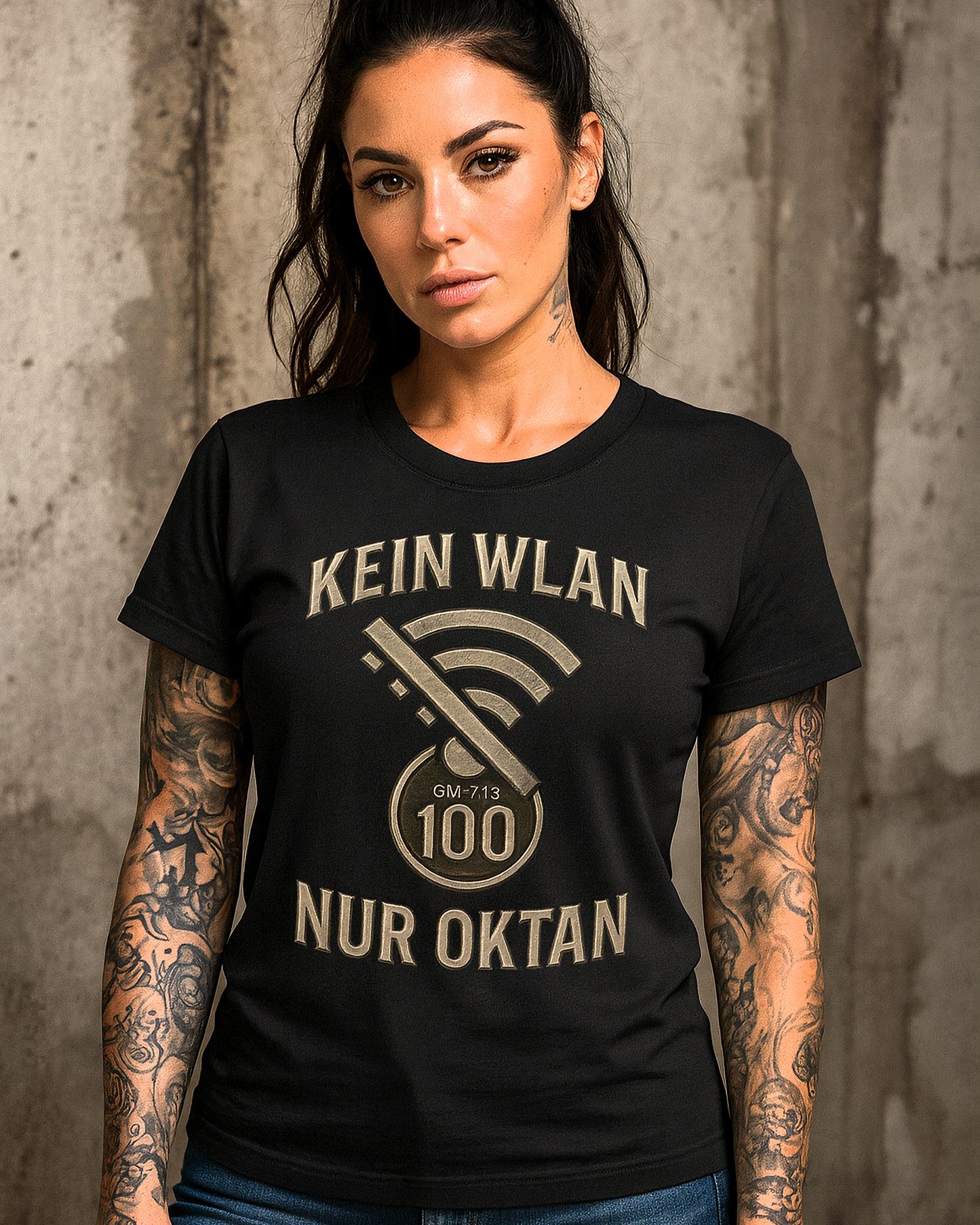 Tattooed woman wearing black Gas Mavericks T-shirt with slogan Kein WLAN Nur Oktan, standing against concrete wall